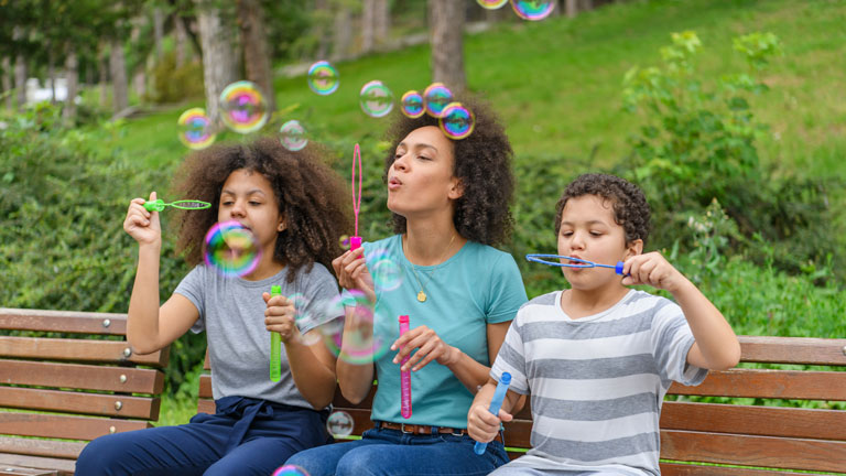 Mom blows bubbles with her kids, a deep breathing moment.